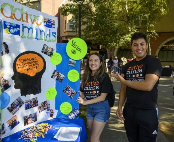 two students standing next to poster at club fair
