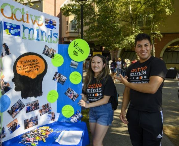 two students standing next to poster at club fair