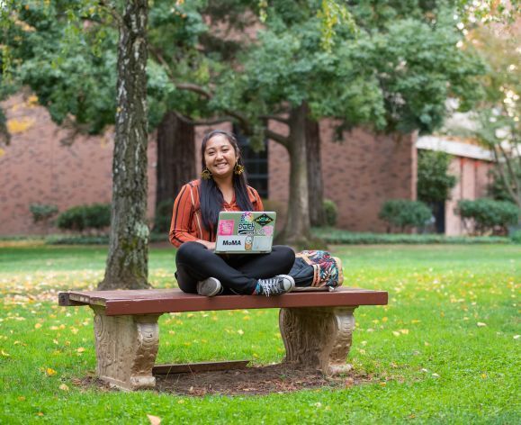 student sitting on a bench outdoors with a laptop