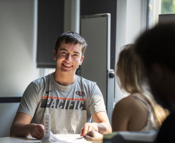student sitting at table with notebook and smiling