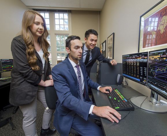 students looking at a computer screen examining stock prices