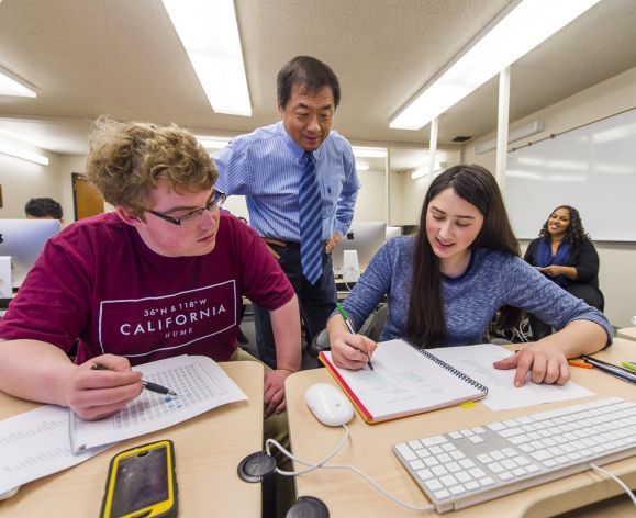 students working at a table with a faculty member helping