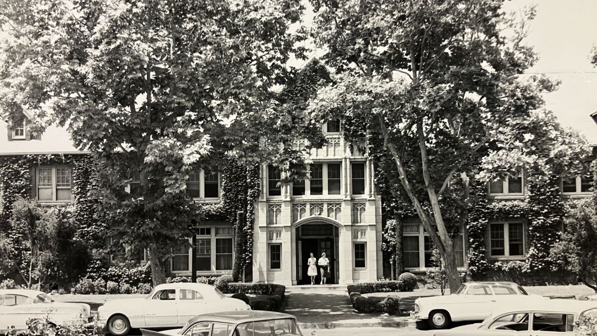 Two people walk out of South Hall toward parked cars. 