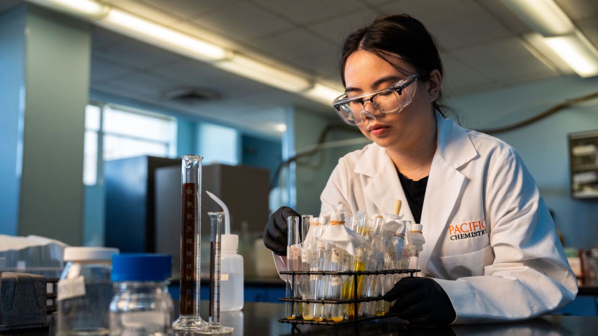 a student in a white coat works at a lab counter