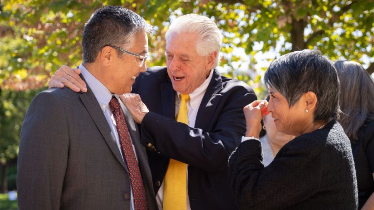 Three people embrace at DeRosa's memorial